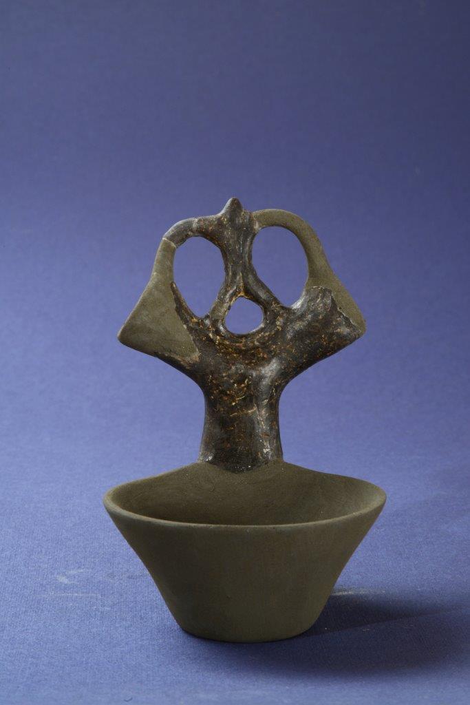 A ‘bucchero’ (dark black earthenware) handle with hollow truncated horns, connected by an openwork motif with a stylized human figure